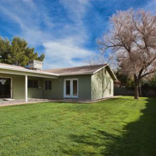 A spacious backyard with a single-story house and well-maintained lawn under a clear blue sky.
