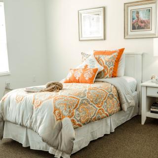 A cozy bedroom with orange accented bedding and framed artwork on the walls.