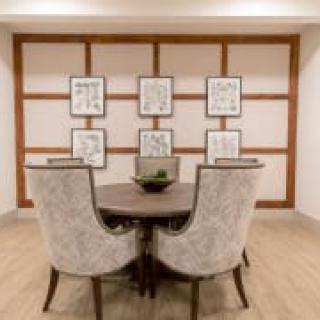 A modern interior space featuring a round table with two upholstered chairs, set against a wall adorned with framed artwork.