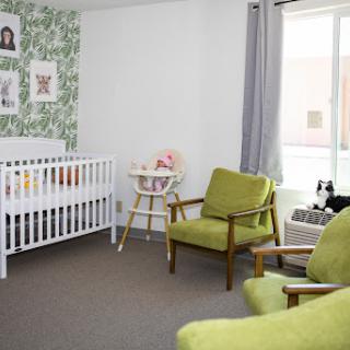 A cozy and stylish nursery featuring a white crib, green chairs, and lovely wall decor.