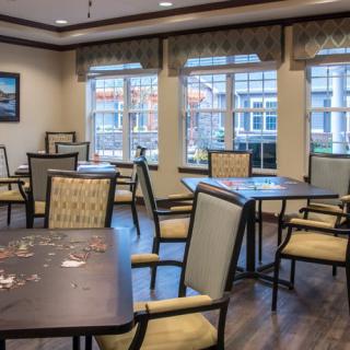 An empty dining room with arranged tables and chairs near large windows.