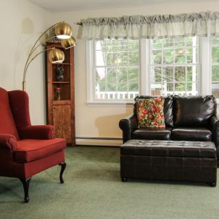 A cozy living room with a red armchair, a leather sofa, and a standing lamp by the window.