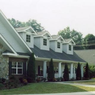 A residential house with a porch and dormer windows, surrounded by trees.