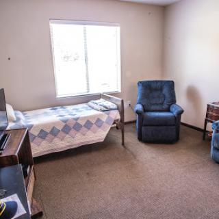 A cozy room featuring a bed, a recliner chair, and ample natural light from the window.
