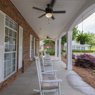A covered porch featuring rocking chairs, ceiling fans, and a brick exterior with lush landscaping.