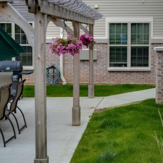 A backyard patio area with a pergola, hanging flowers, and outdoor seating.