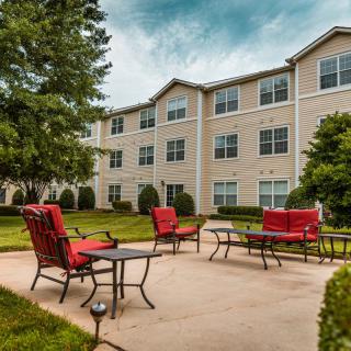 A well-maintained patio area with red chairs in front of a residential apartment building, surrounded by lush greenery.