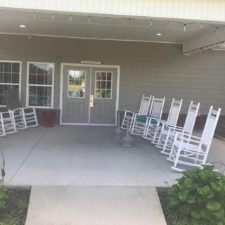 A row of white rocking chairs lined up on a front porch outside a building entrance.