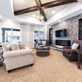 A modern living room featuring a comfortable seating area with a sofa and armchairs, stylish coffee table, and a stone accent wall with a mounted television. The space is complemented by exposed beams on the ceiling.