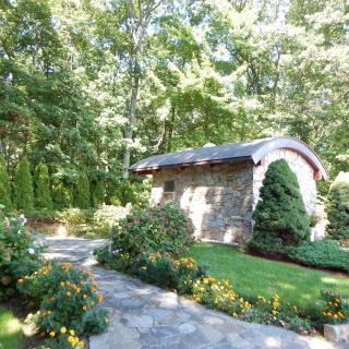 A peaceful garden scene with a stone building surrounded by lush greenery and flowers.