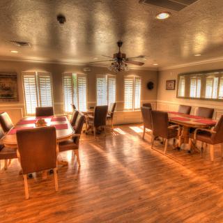 A warmly lit dining room with wooden floors, several tables, and chairs arranged around the room.