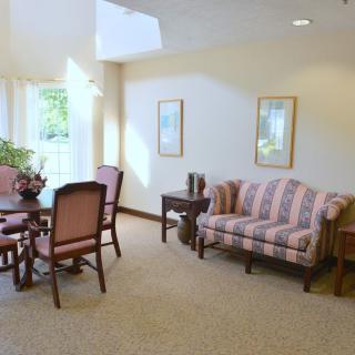 A cozy living room with a striped sofa, chairs around a wooden table, and natural light streaming in through the window.