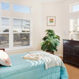 A cozy bedroom with a bed, dresser, and a large window letting in natural light.
