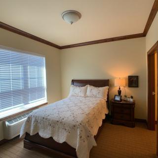 A cozy bedroom with a neatly made bed next to a window and a nightstand with a lamp.