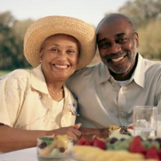 A smiling couple enjoying a picnic outdoors with an assortment of fruits.