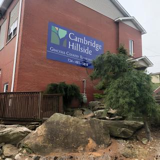 A brick building with a sign reading 'Cambridge Hillside' surrounded by rocks and greenery.