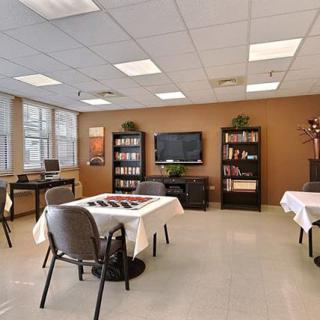 A well-lit meeting room with tables and chairs arranged, featuring a television and bookshelves against the walls.