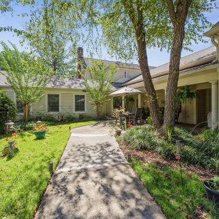 A beautiful home with a lush garden and trees lining the pathway.