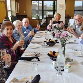 A group of elderly people enjoying a celebratory meal together, raising their glasses at a beautifully set dining table with floral decorations.