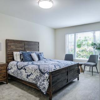 A cozy and modern bedroom featuring a wooden bed frame, decorative bedding, and natural light from a nearby window.