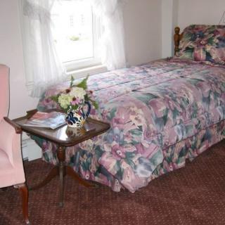 A cozy bedroom with a floral bedspread, an armchair, and a side table next to a window.