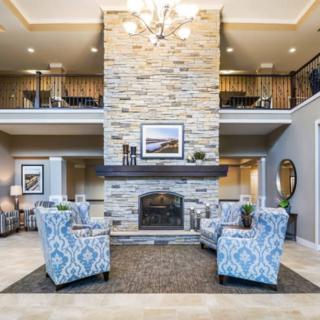 A spacious living room with a stone fireplace, patterned armchairs, and a chandelier creating a cozy atmosphere.