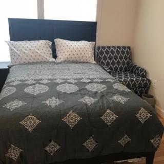 A cozy bedroom setup with a bed, patterned bedding, pillows, and an adjacent armchair.