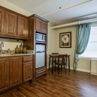 A cozy kitchen and dining area with wooden cabinets and flooring, accompanied by a small dining table near a curtained window.