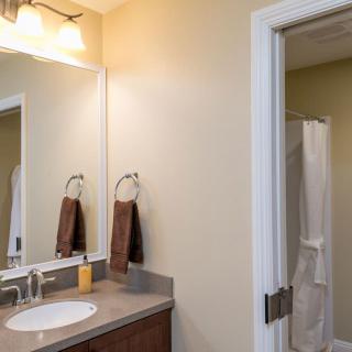 A clean bathroom featuring a sink with a mirror, towels on rings, and a view of a shower through an open doorway.