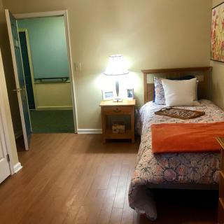 A cozy bedroom with a single bed and a nightstand, softly lit by a lamp.