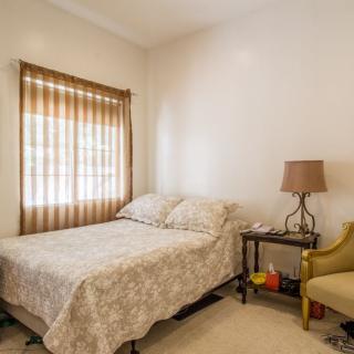 A cozy bedroom with a neatly made bed, a lamp on a nightstand, and a comfortable chair beside the window.