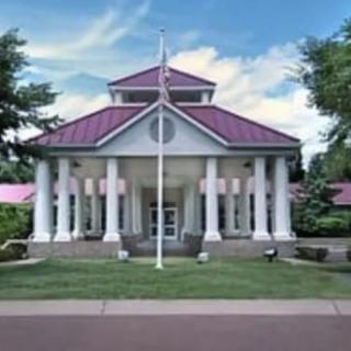 A symmetrical building with columns and a purple roof, surrounded by trees.