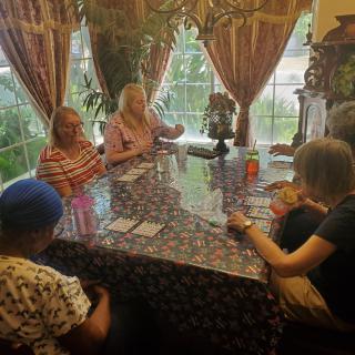A group of people sitting around a table playing cards near a window with curtains.