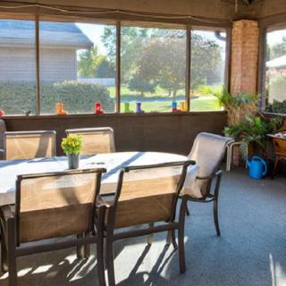 A sunny screened porch with a dining table and chairs, decorated with plants.