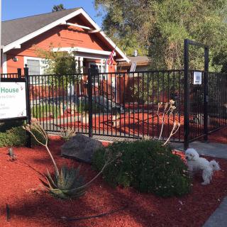 A charming red brick house with a fenced garden and landscaping, featuring a sign and a small dog in the yard.