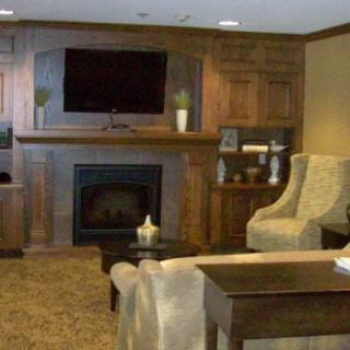 A cozy living room featuring a fireplace and wood paneling with a television mounted above.