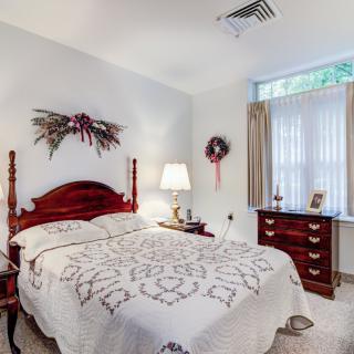 A cozy bedroom with traditional decor featuring a quilted bedspread, wooden furniture, and floral decorations.