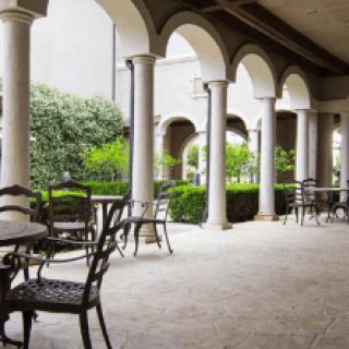 A tranquil patio with arched columns, tables, and chairs overlooking a lush garden.