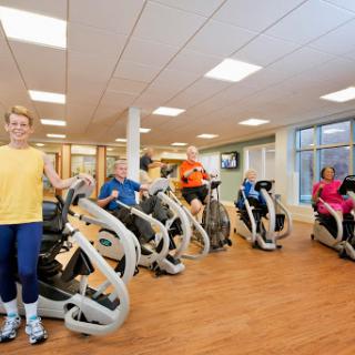 A vibrant gym scene featuring individuals engaged in a group workout session on exercise machines.