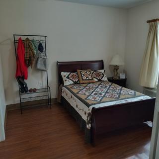 A cozy bedroom with a bed, clothing rack, and a lamp by the window.