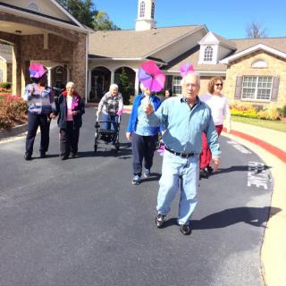 A group of seniors enjoying a sunny day walk, carrying colorful flags outside a residential building.