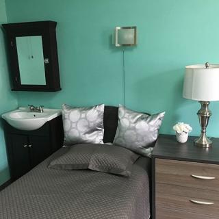 A small bedroom with a single bed, bedside cabinet, lamp, and wall-mounted sink.