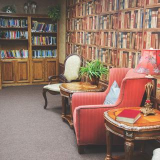 A cozy library corner with bookshelves, an armchair, and a lamp.