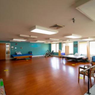 A spacious interior room with wooden flooring, containing tables and chairs, well-lit by ceiling lights.