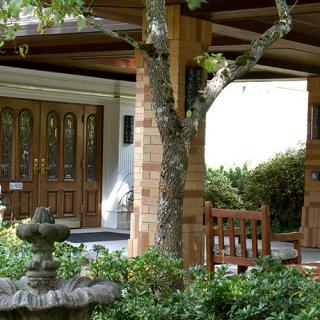 A cozy porch with wooden doors, surrounded by a lush garden and a small fountain.