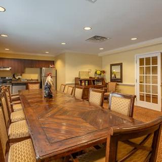 A spacious dining room with a large wooden table and chairs, adjacent to a kitchen area.