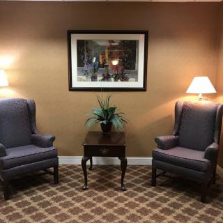 A cozy waiting room with two armchairs, a small table, lamps, and artwork on the wall.