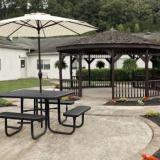 A peaceful outdoor patio area with a gazebo, picnic table, and umbrella in a garden setting.
