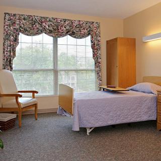A hospital room with a single bed, chair, and large window with patterned curtains.