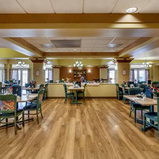 A spacious dining room with wooden floors, neatly arranged tables and chairs, and elegant lighting fixtures.